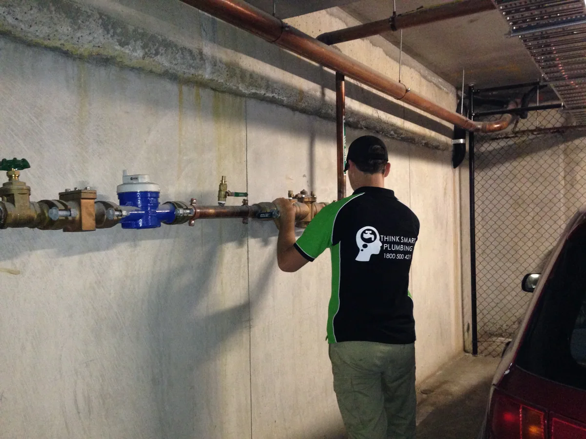 Plumber working on exposed copper pipework and valves along a concrete wall