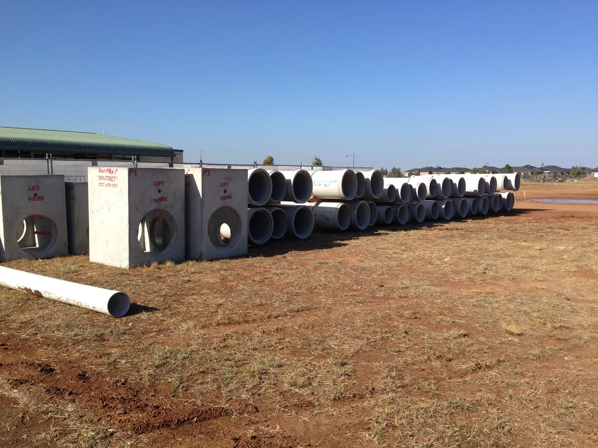Concrete drainage pits and large pipes laid out beside a construction site