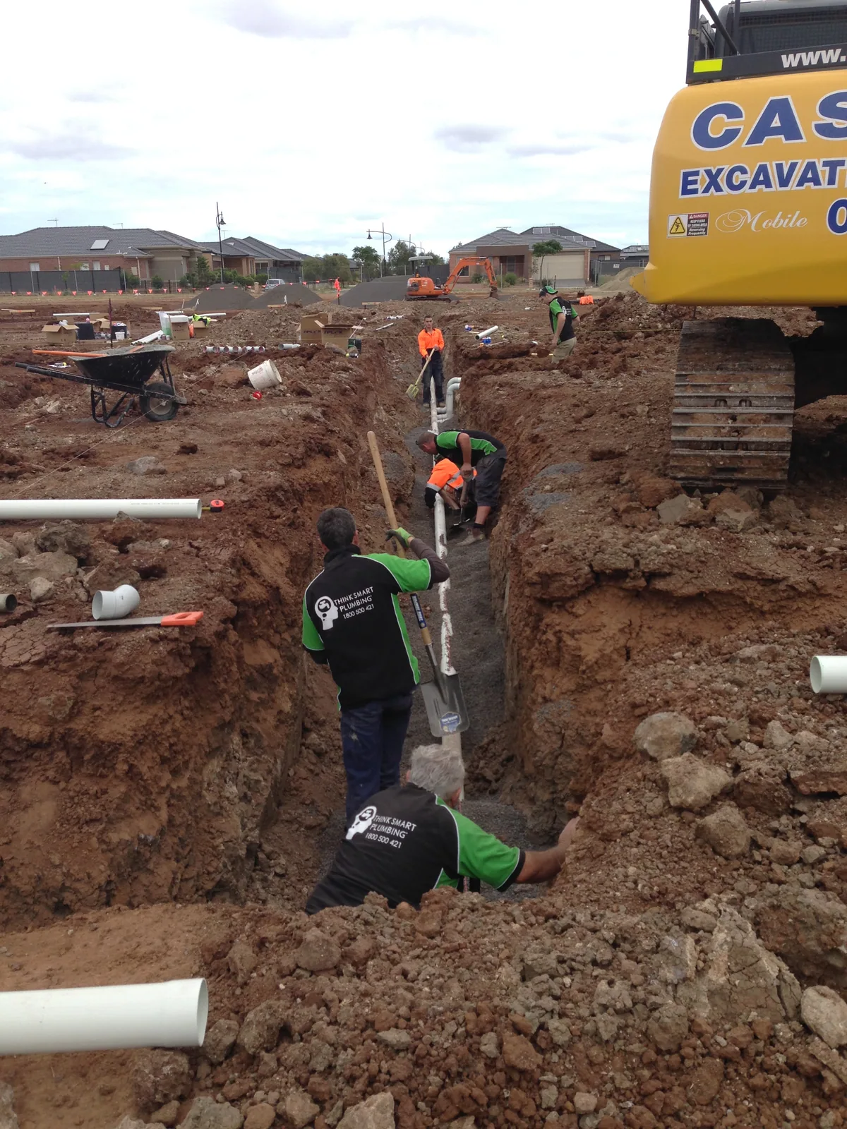 Think Smart Plumbing crew laying white pipework in a long excavated trench