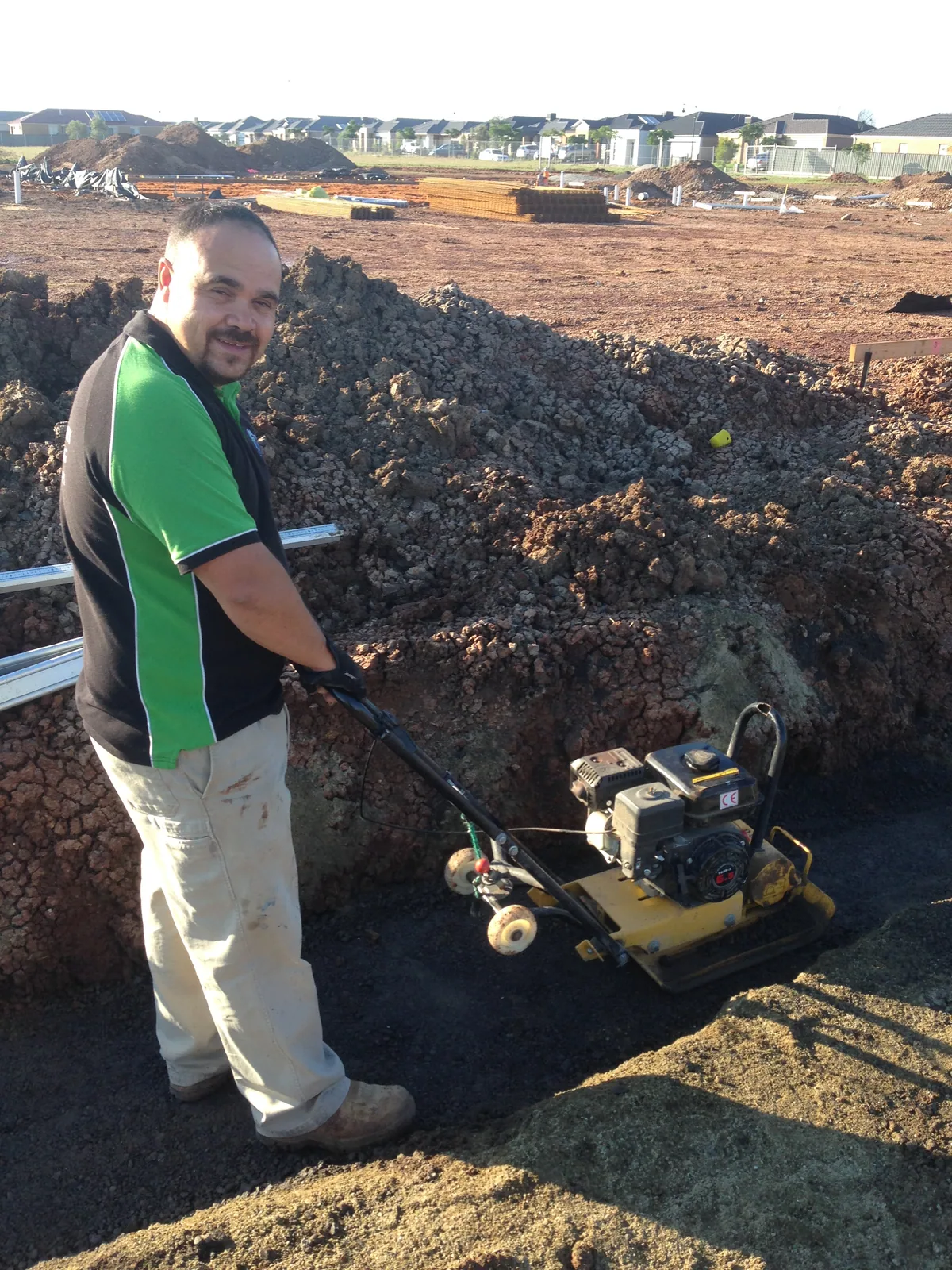 Plumber using a plate compactor on the bedding in an excavated trench