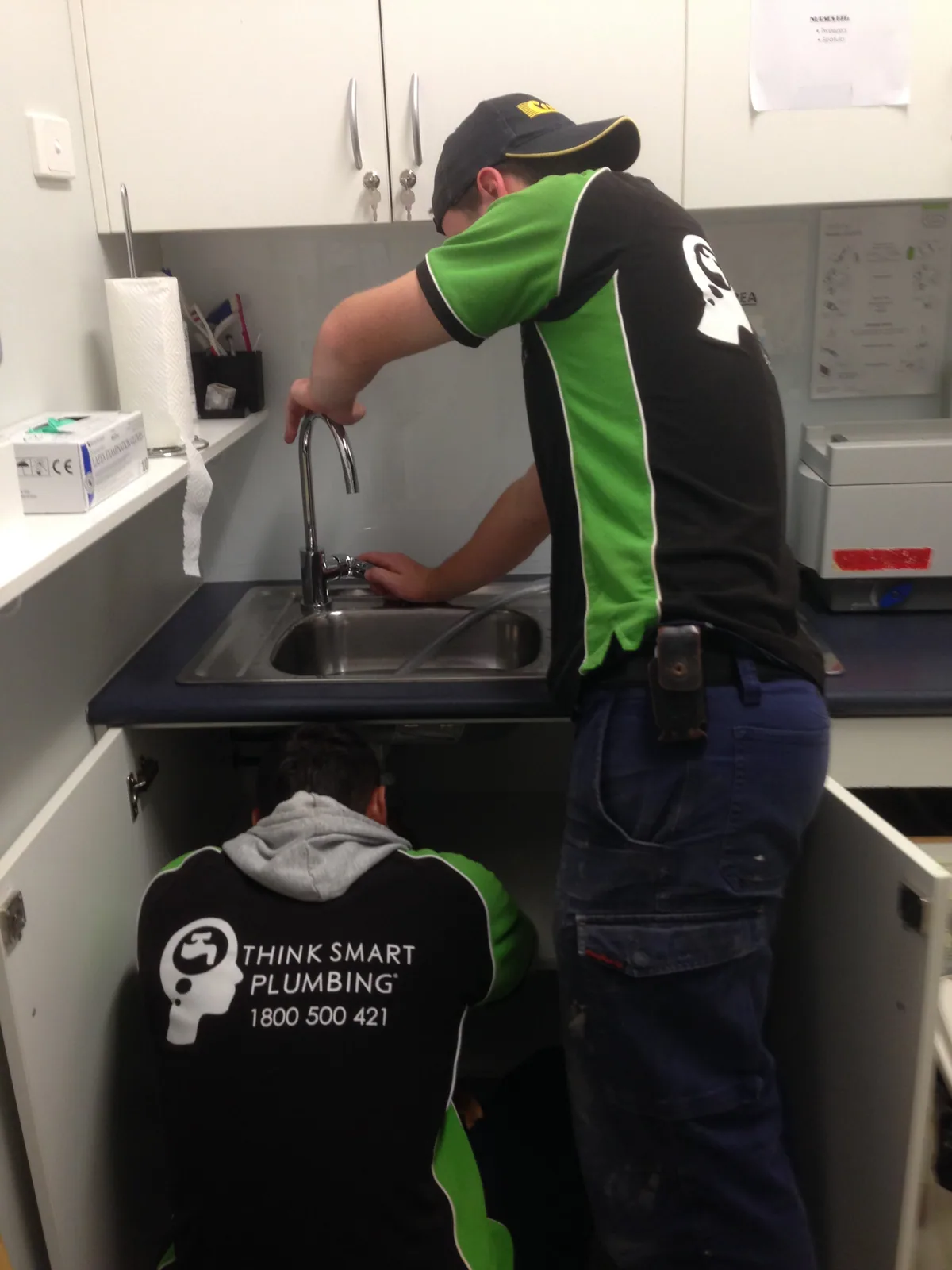 Two Think Smart Plumbing workers fitting a kitchen tap and working below the sink