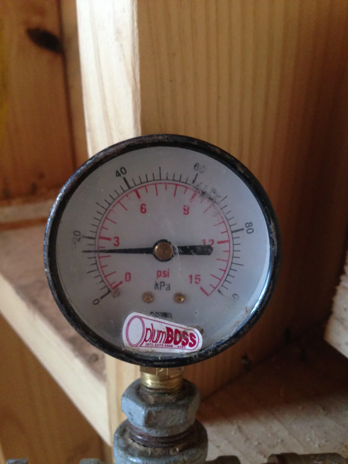 Close-up of a plumbing pressure gauge beside timber framing