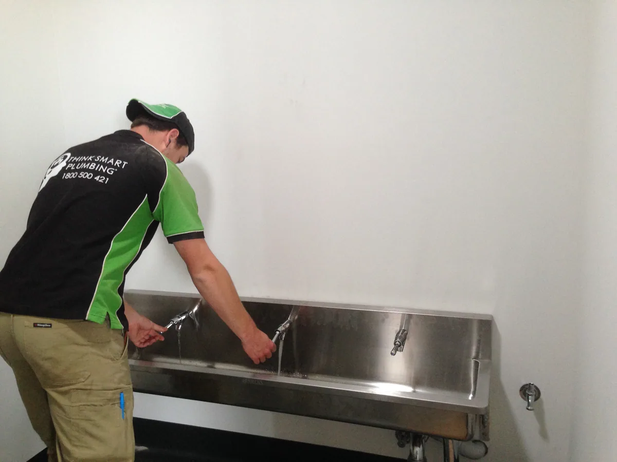 Think Smart Plumbing worker checking taps over a stainless-steel trough basin