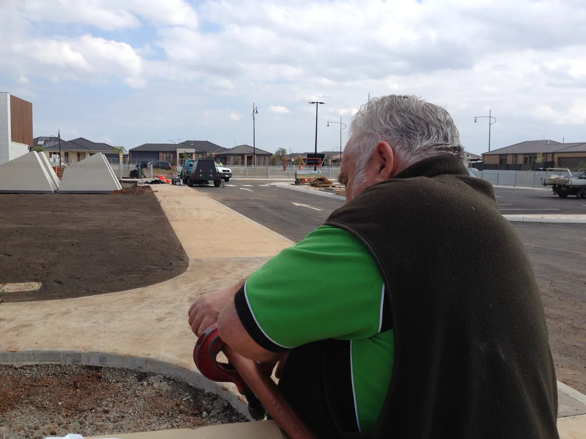 Team member in a green work shirt and dark vest beside pipework on an outdoor construction site